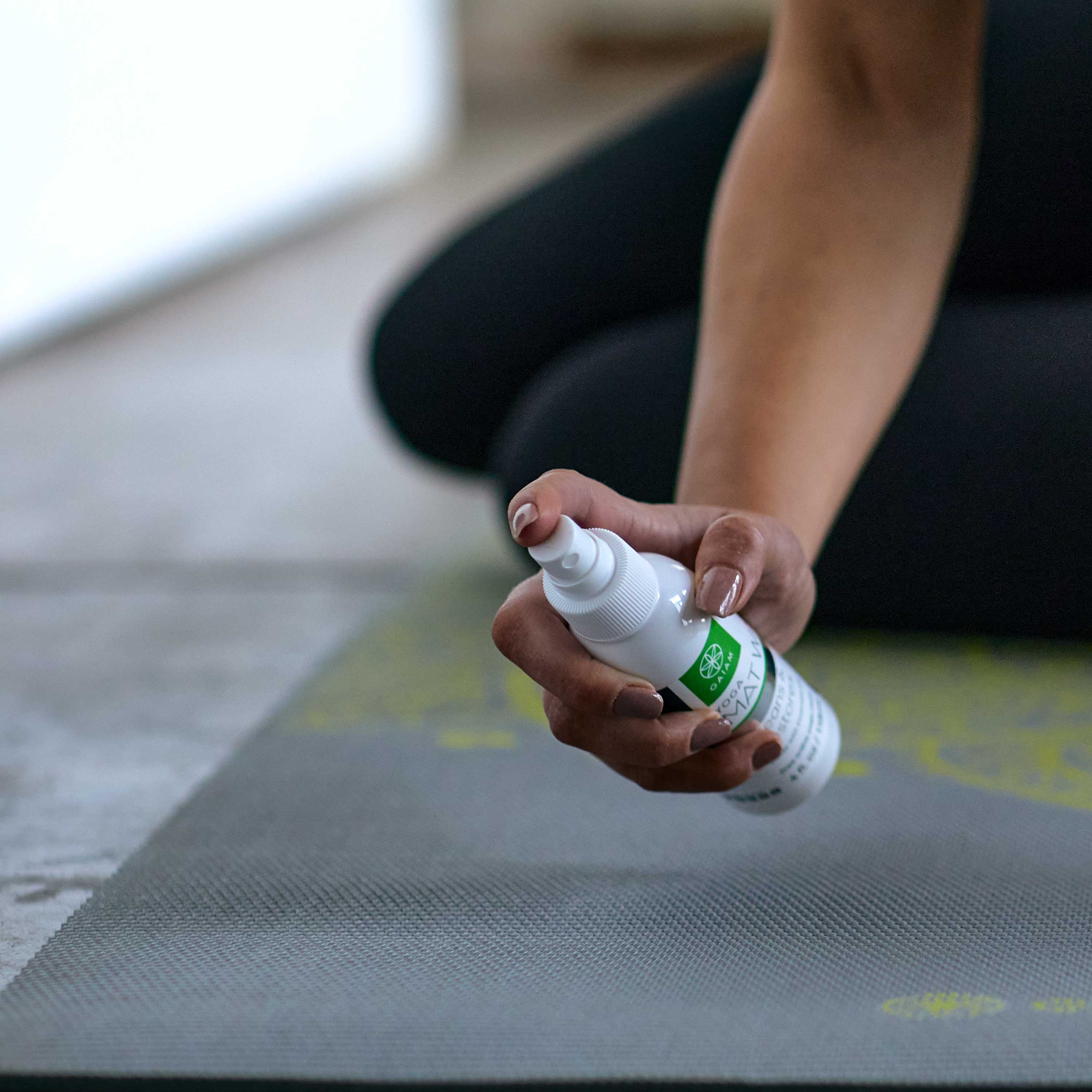 Person spraying mat wash on yoga mat